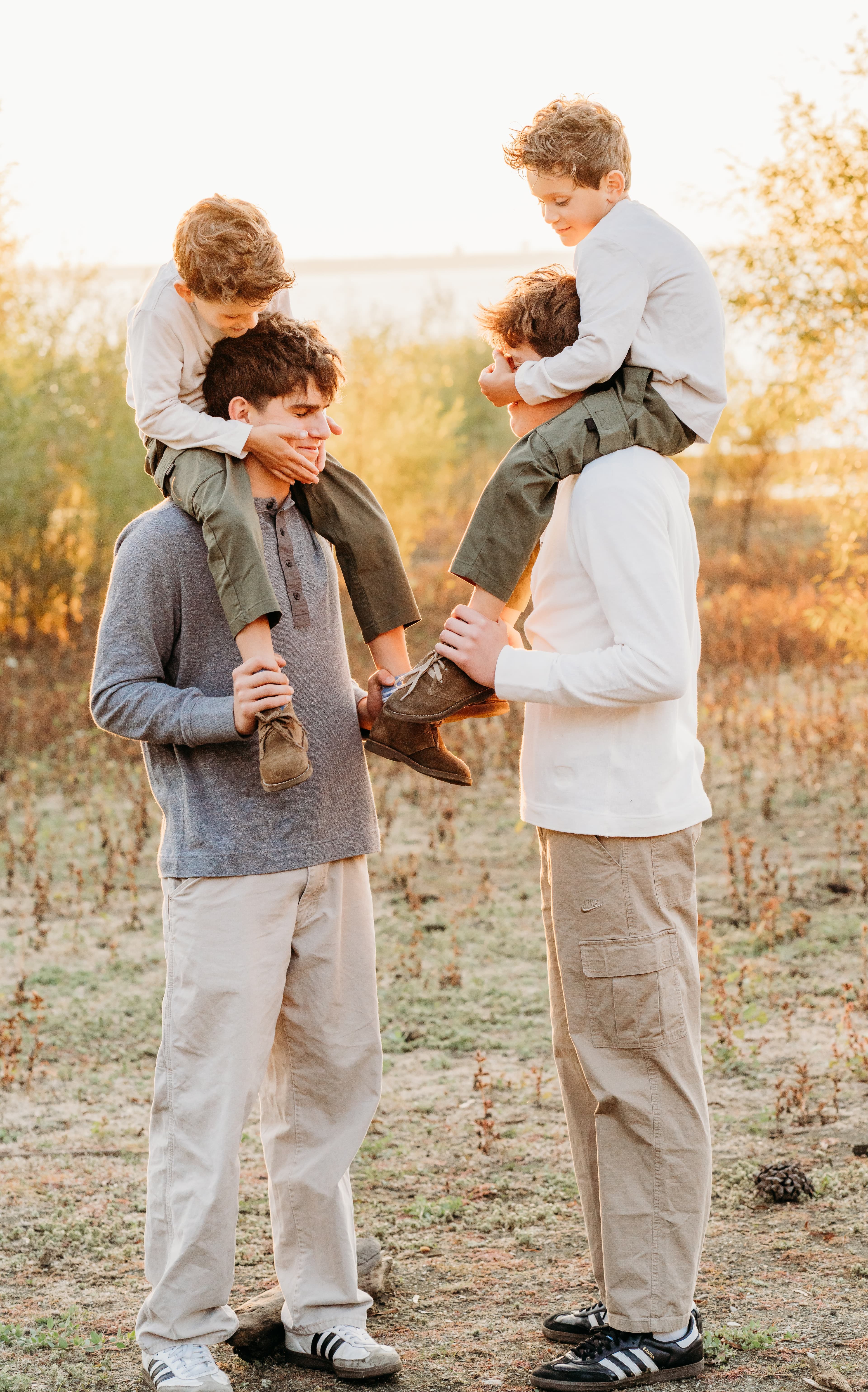 Two young men carry two boys on their shoulders in a golden sunset field