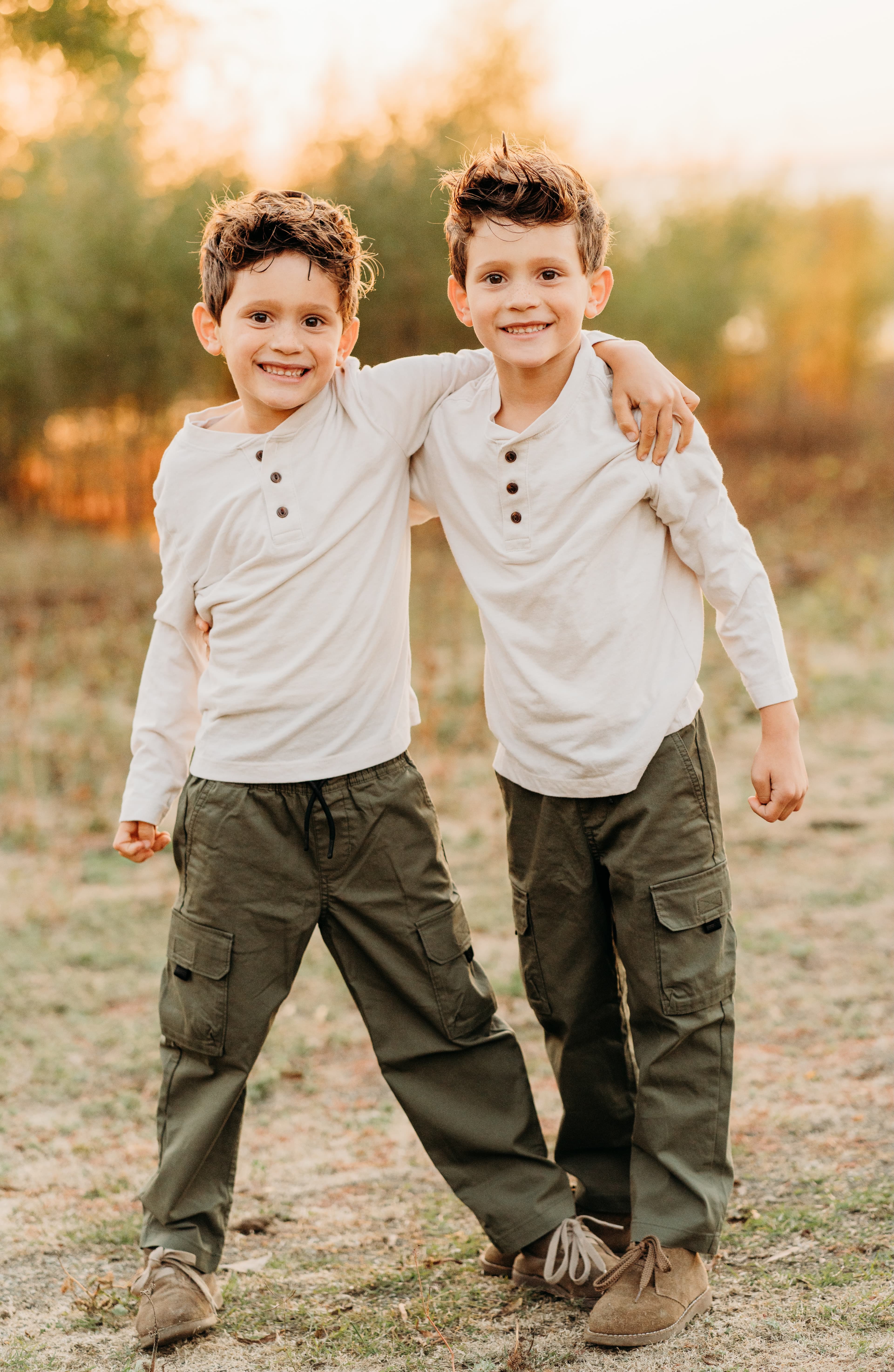 Two young brothers in matching outfits stand arm in arm, smiling at the camera