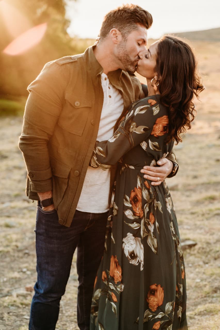 Couple kisses in golden sunset light, she in an olive floral dress