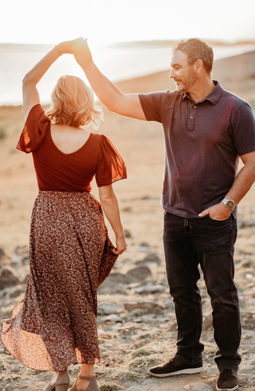 Couple dances on a beach, he twirling her in a rust floral dress