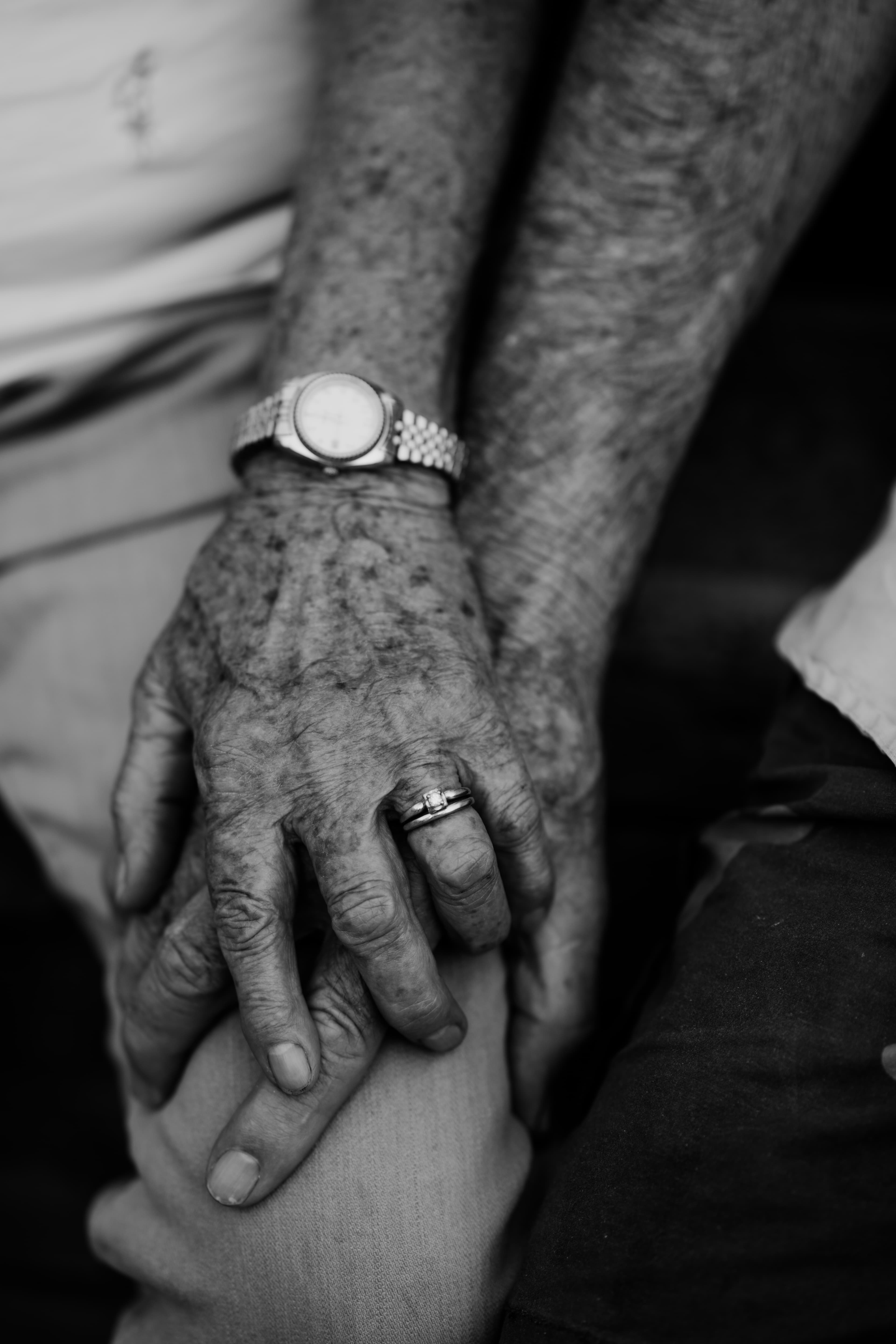 Black-and-white close-up of an elderly couple's clasped hands and rings