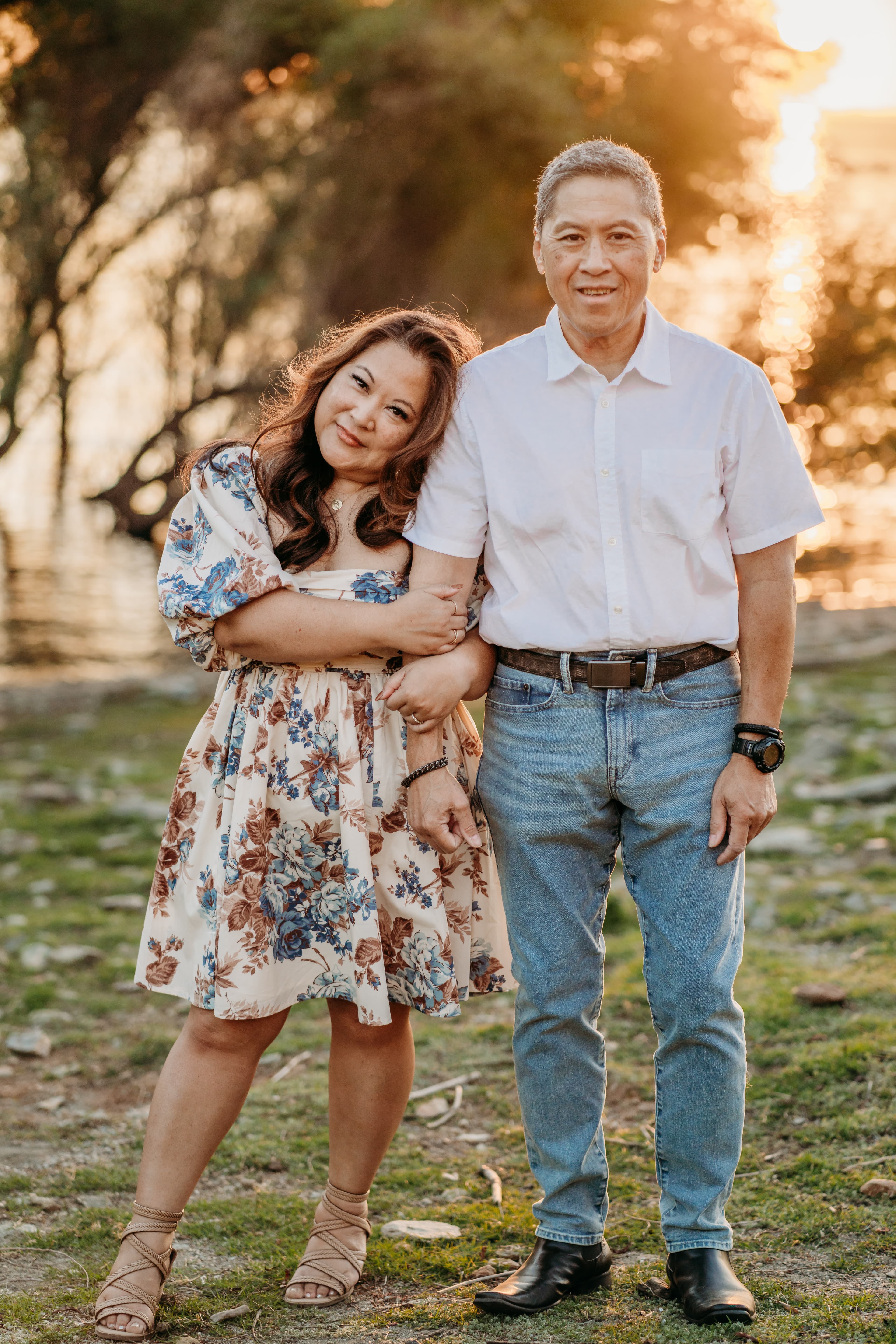 Older couple embraces by the lake at sunset, smiling at the camera