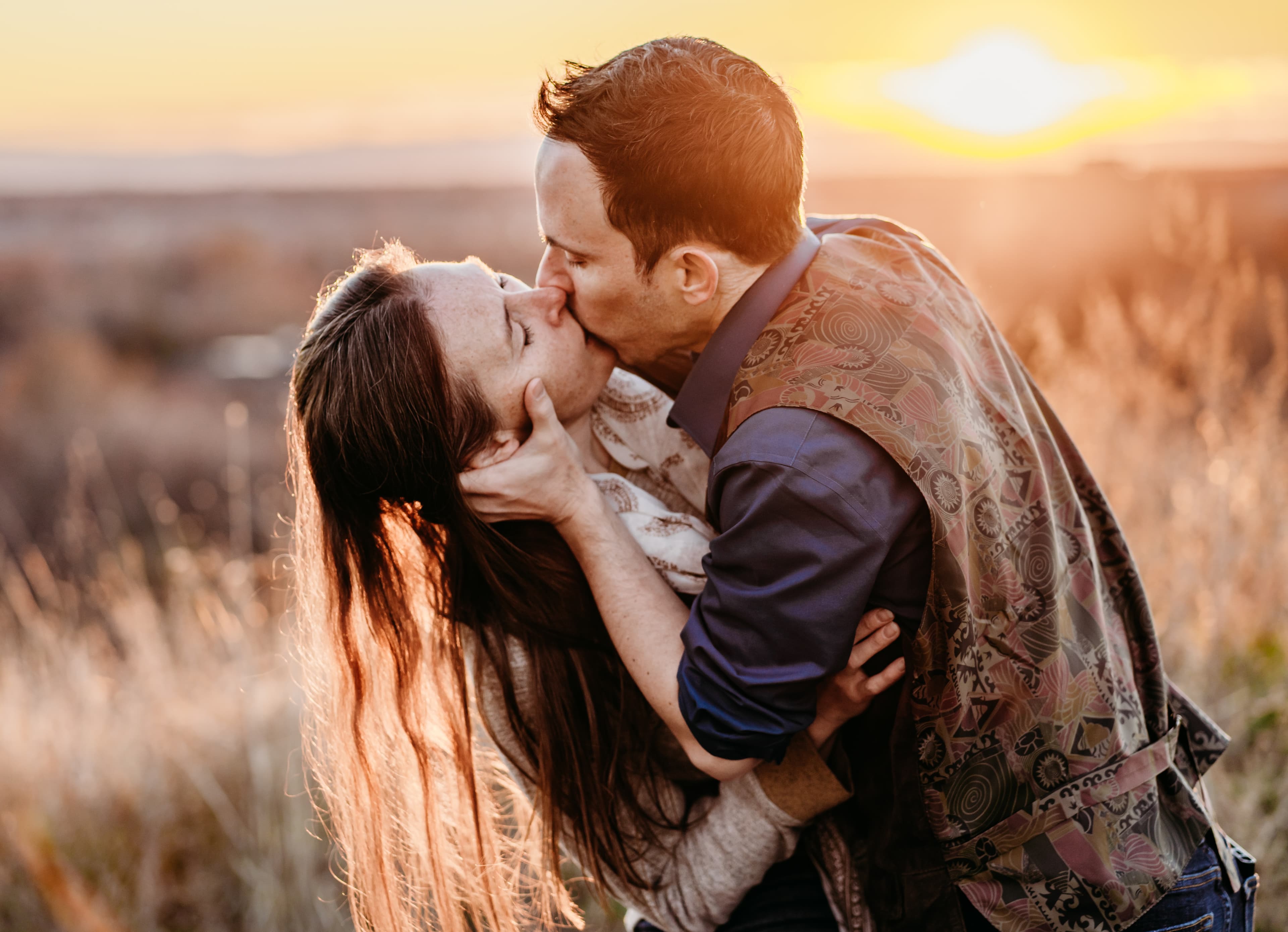 Couple embraces and kisses in a golden field bathed in sunset light