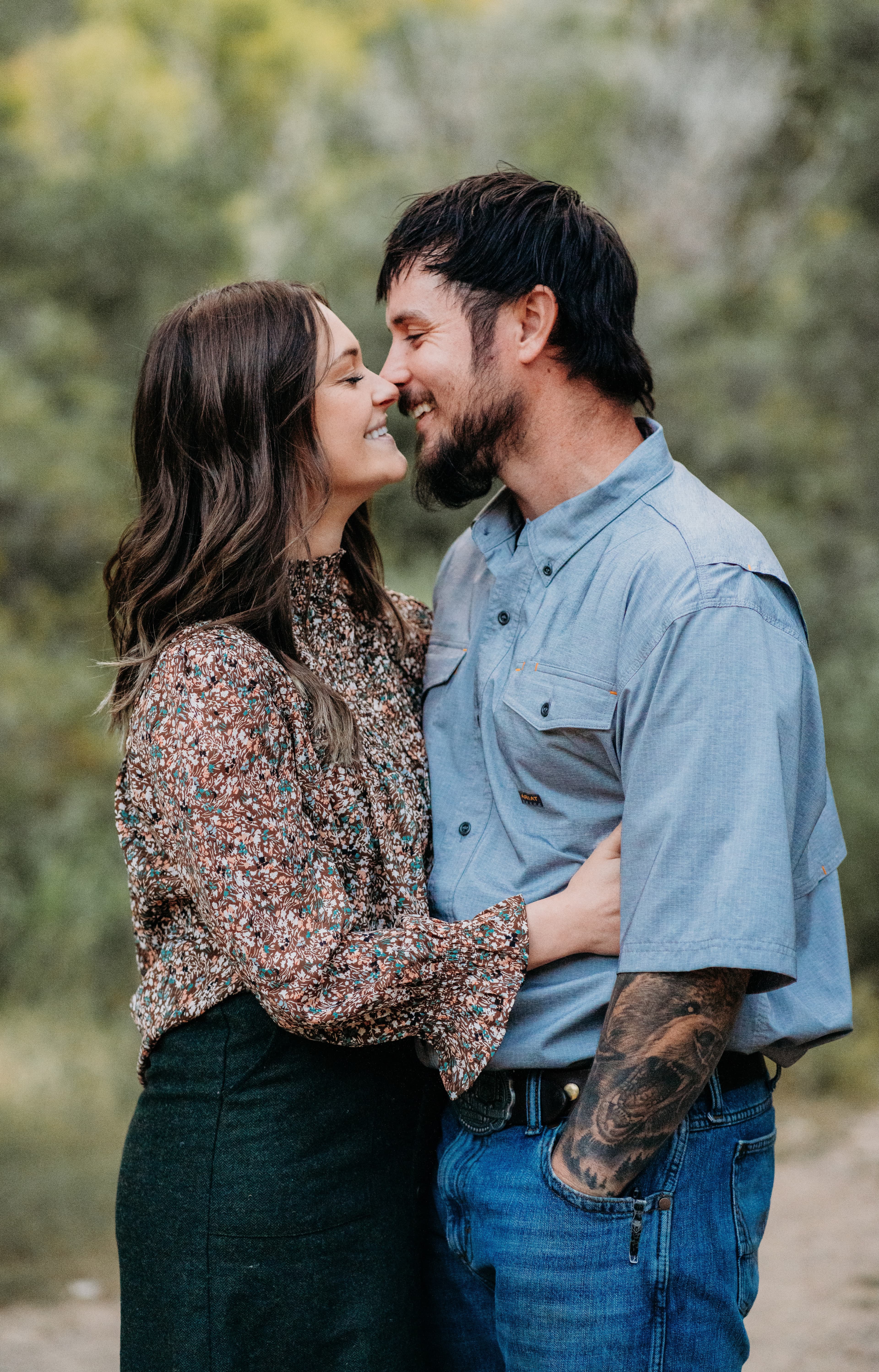 Couple laughs nose to nose surrounded by green foliage
