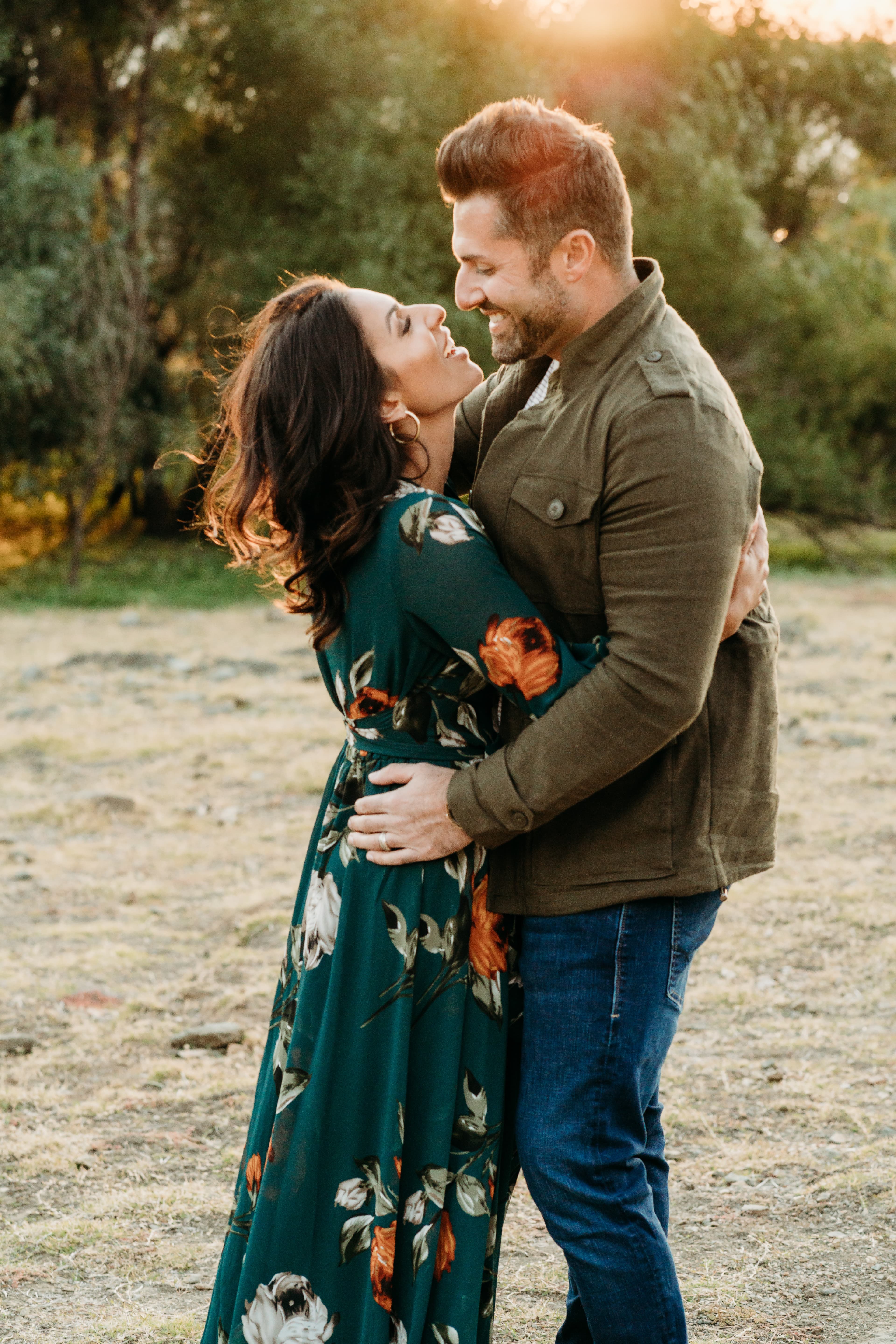 Couple embraces face to face at golden hour, she in a teal floral dress