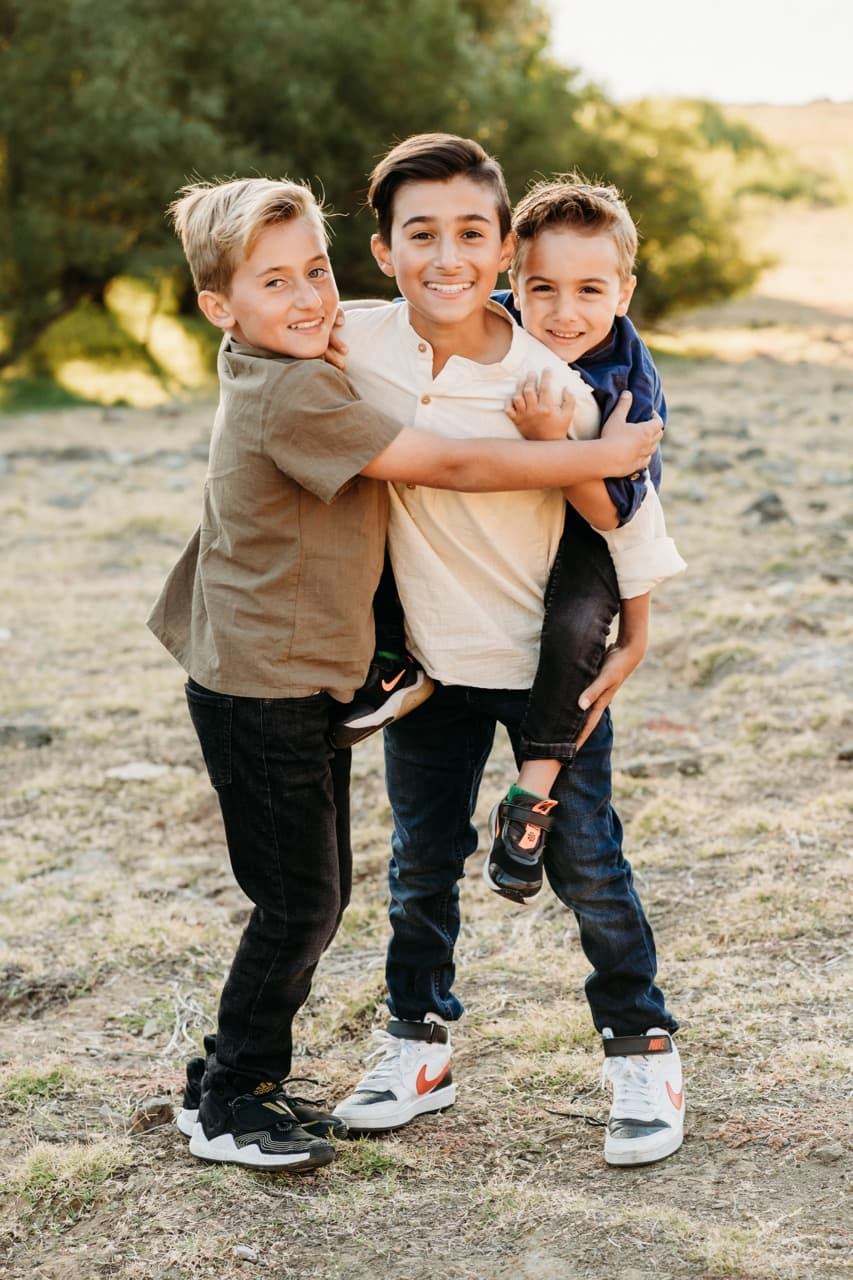 Three brothers pile together laughing, the oldest carrying two younger boys