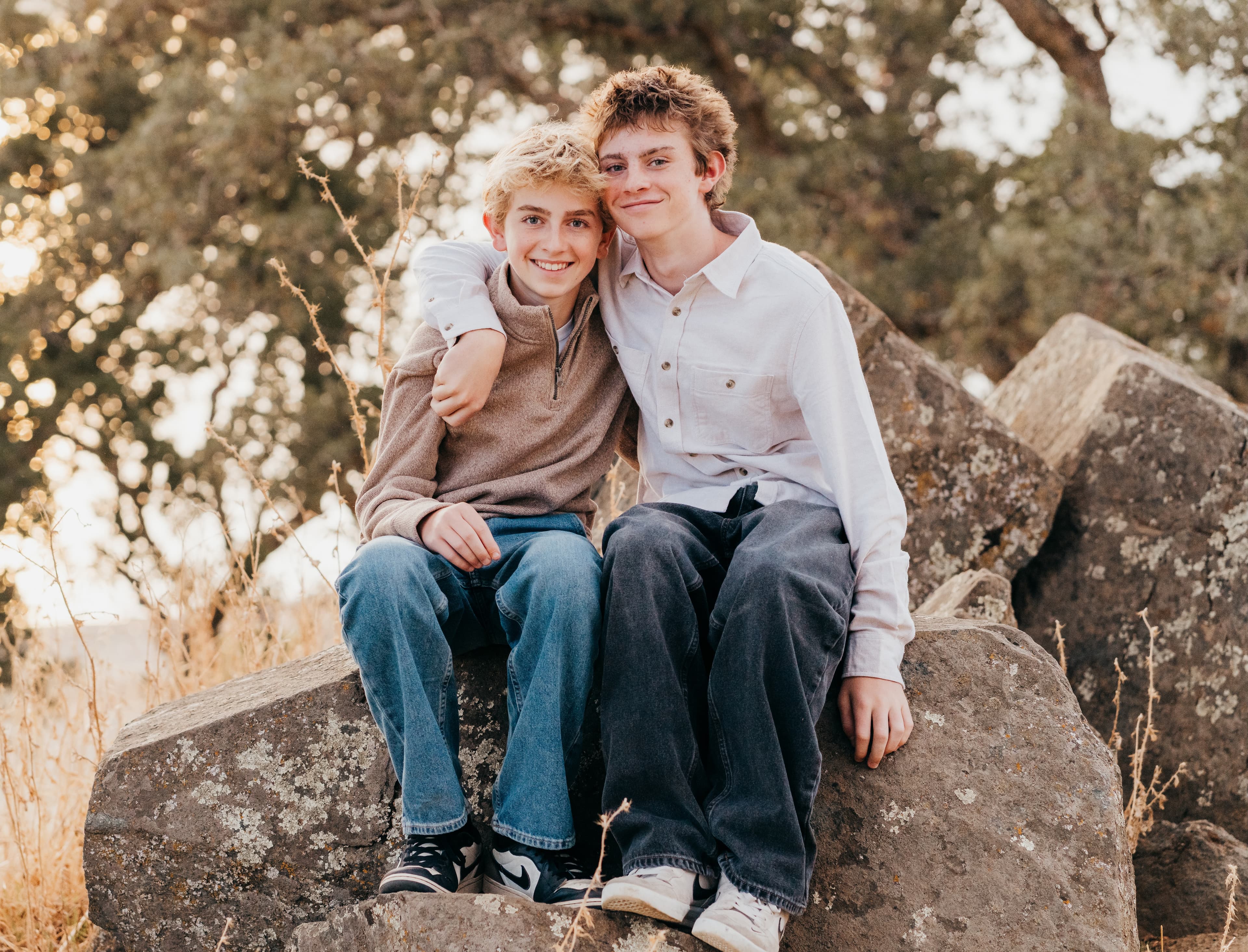 Two teen brothers sit together on boulders, one's arm around the other's shoulder