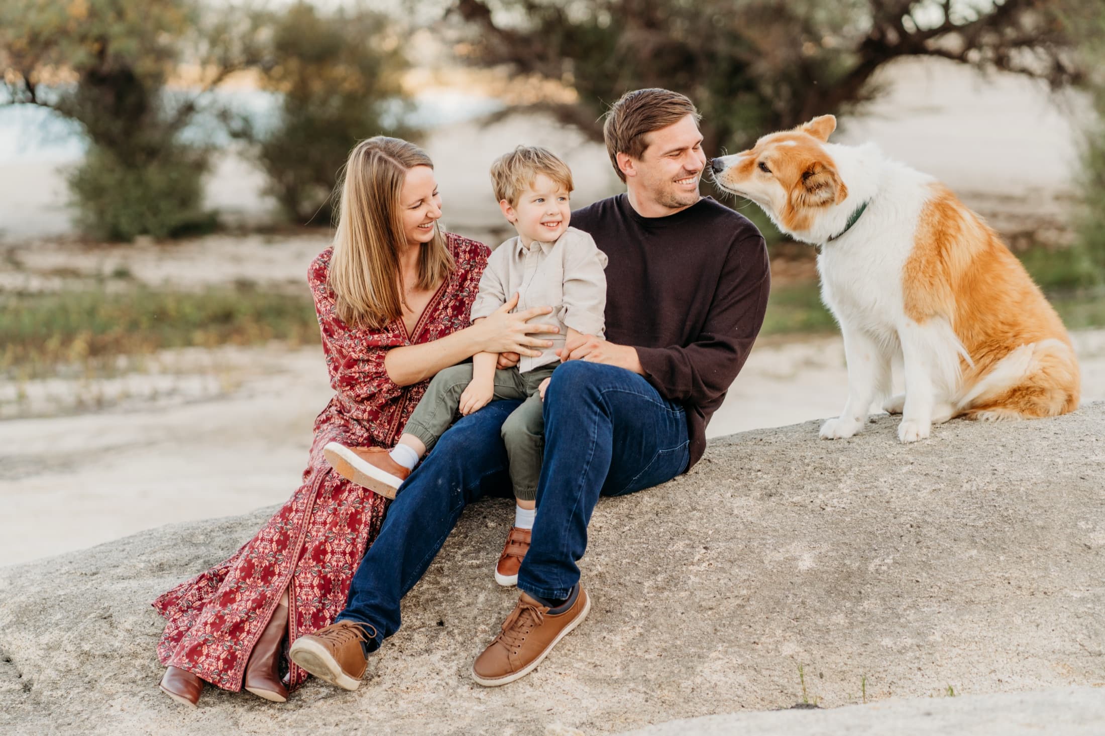 Family sitting on a rock with their corgi nuzzling dad's chin