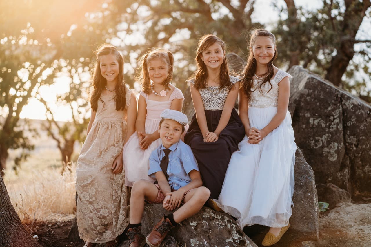 Five cousins dressed up and smiling together on a boulder at golden hour