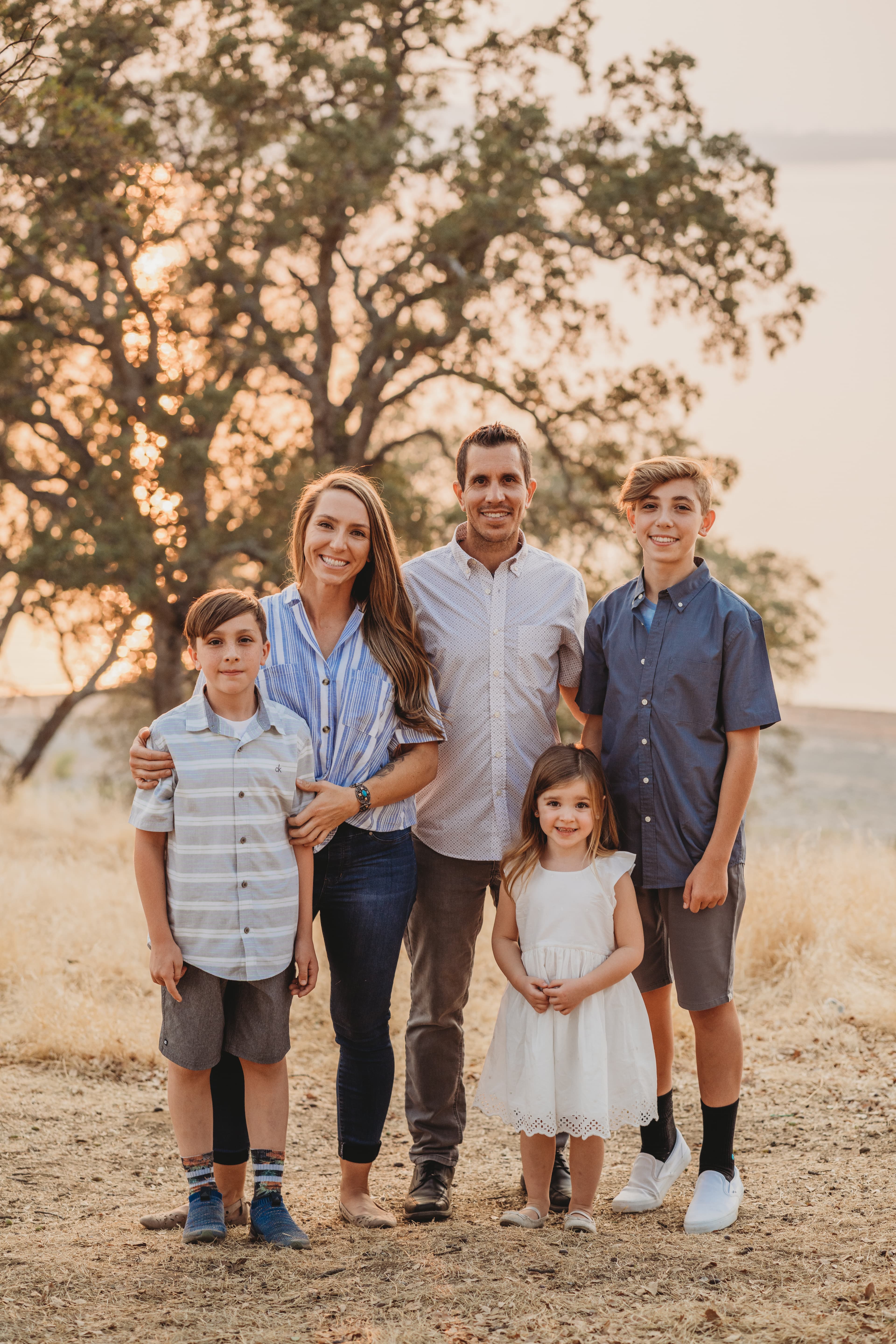 Family of five smiling together in golden grass at sunset by a lake
