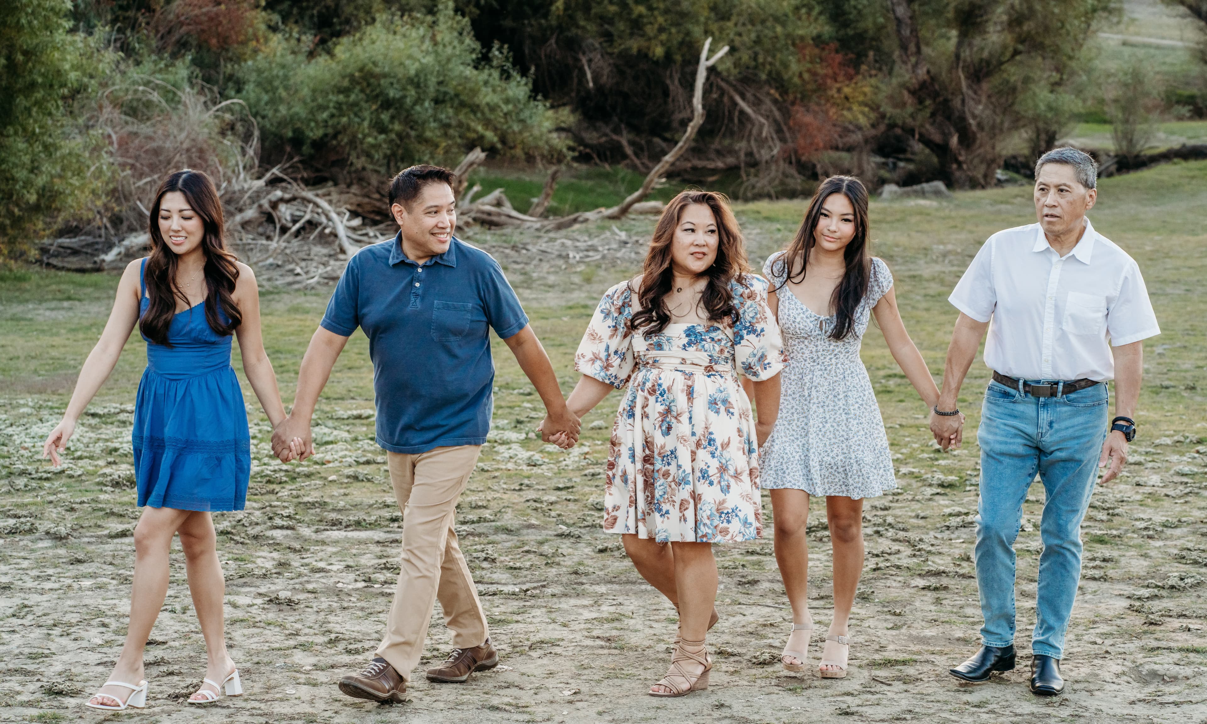 Five family members walk hand in hand across a dry grassy field, smiling