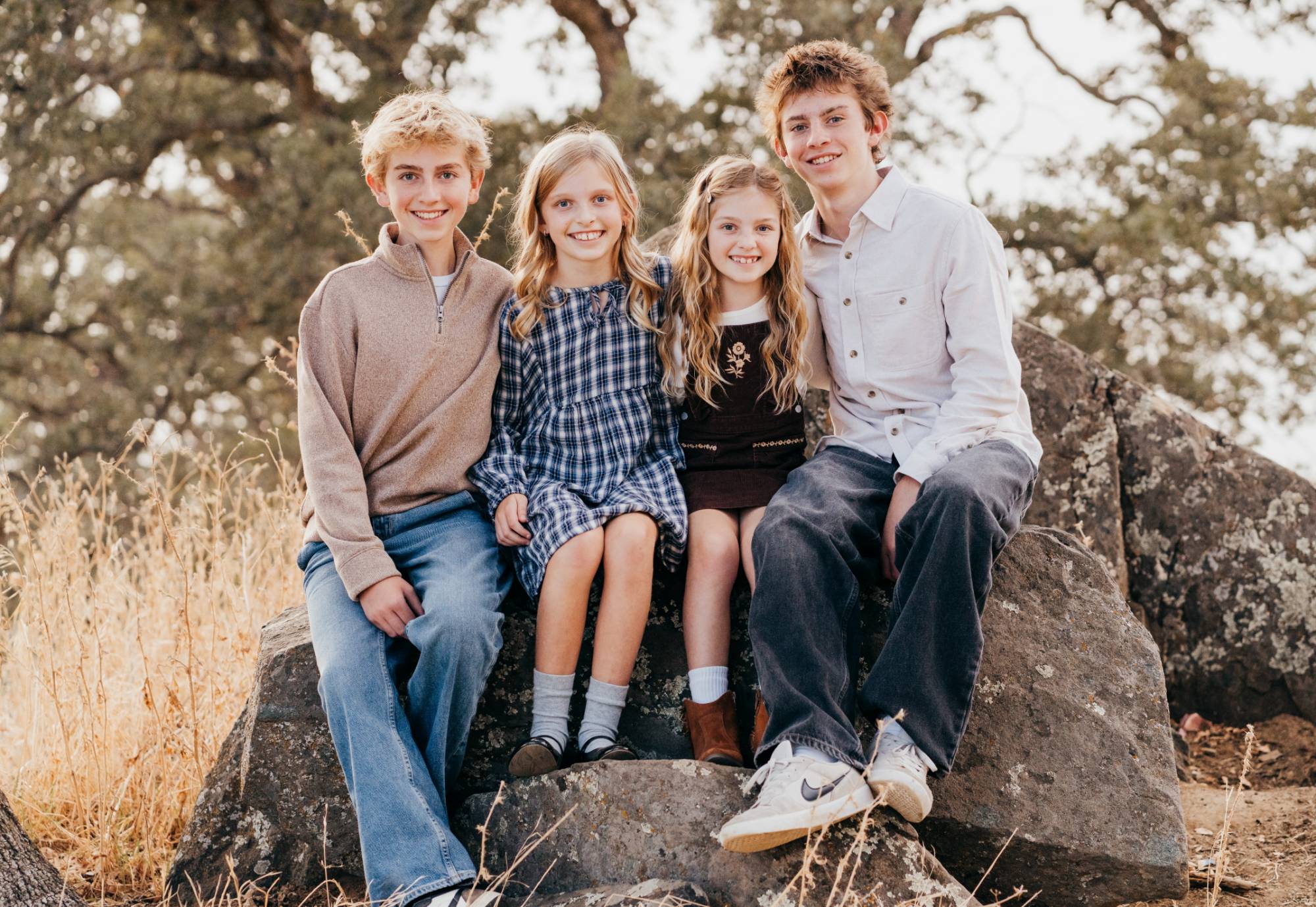 Four siblings sit together on a boulder, arms around each other, smiling