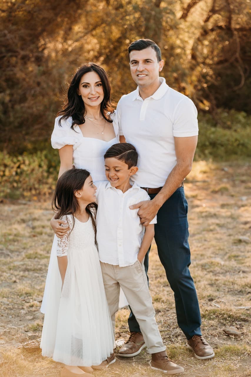 Family of four in white outfits smiling together outdoors at sunset