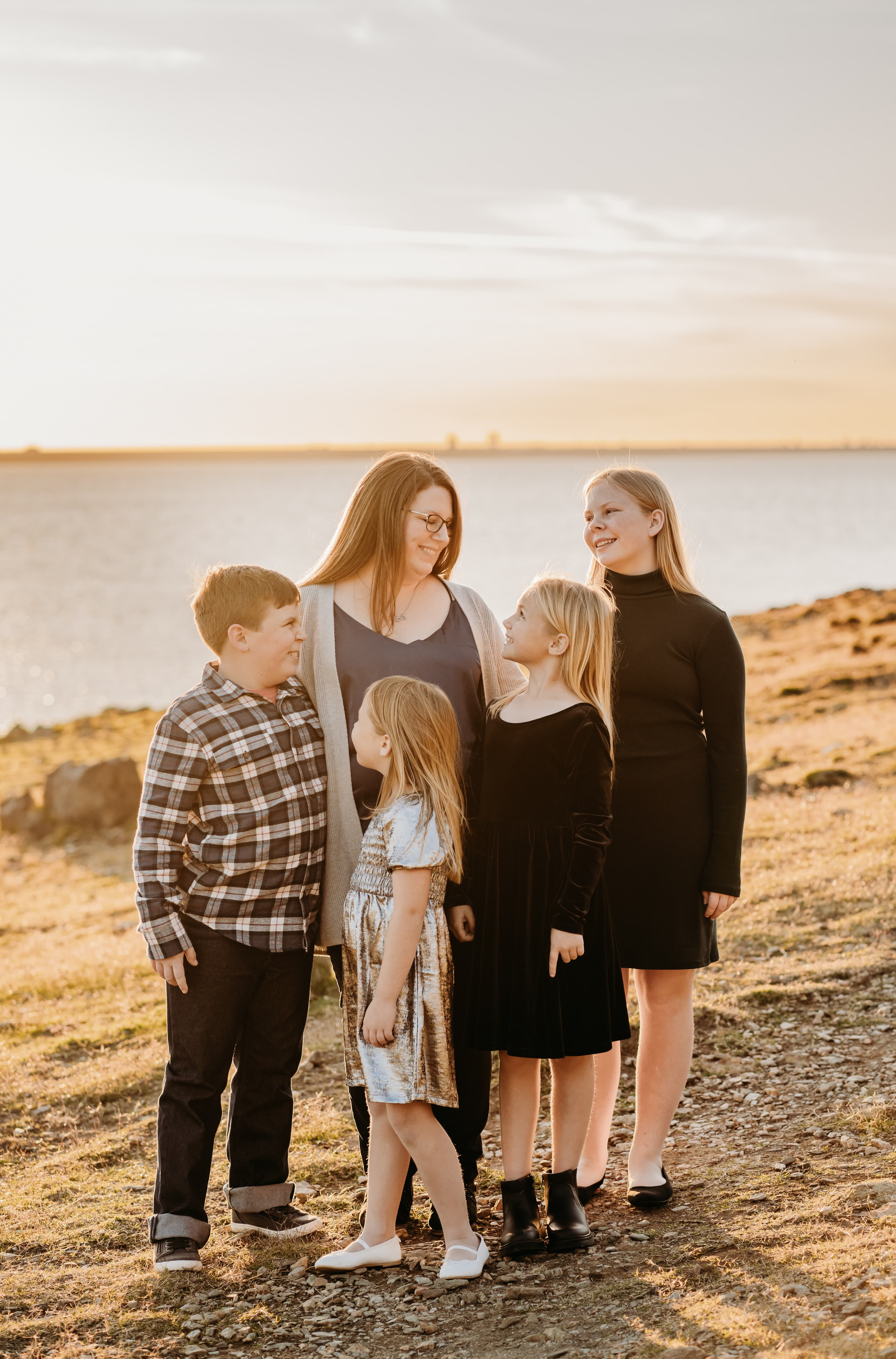 Mother and her four children share a warm moment together on a rocky lakeshore at sunset