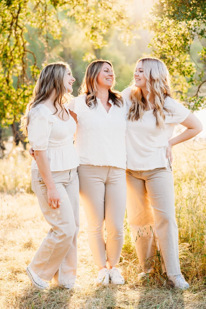 Mother and two daughters in matching white tops and tan pants laugh together