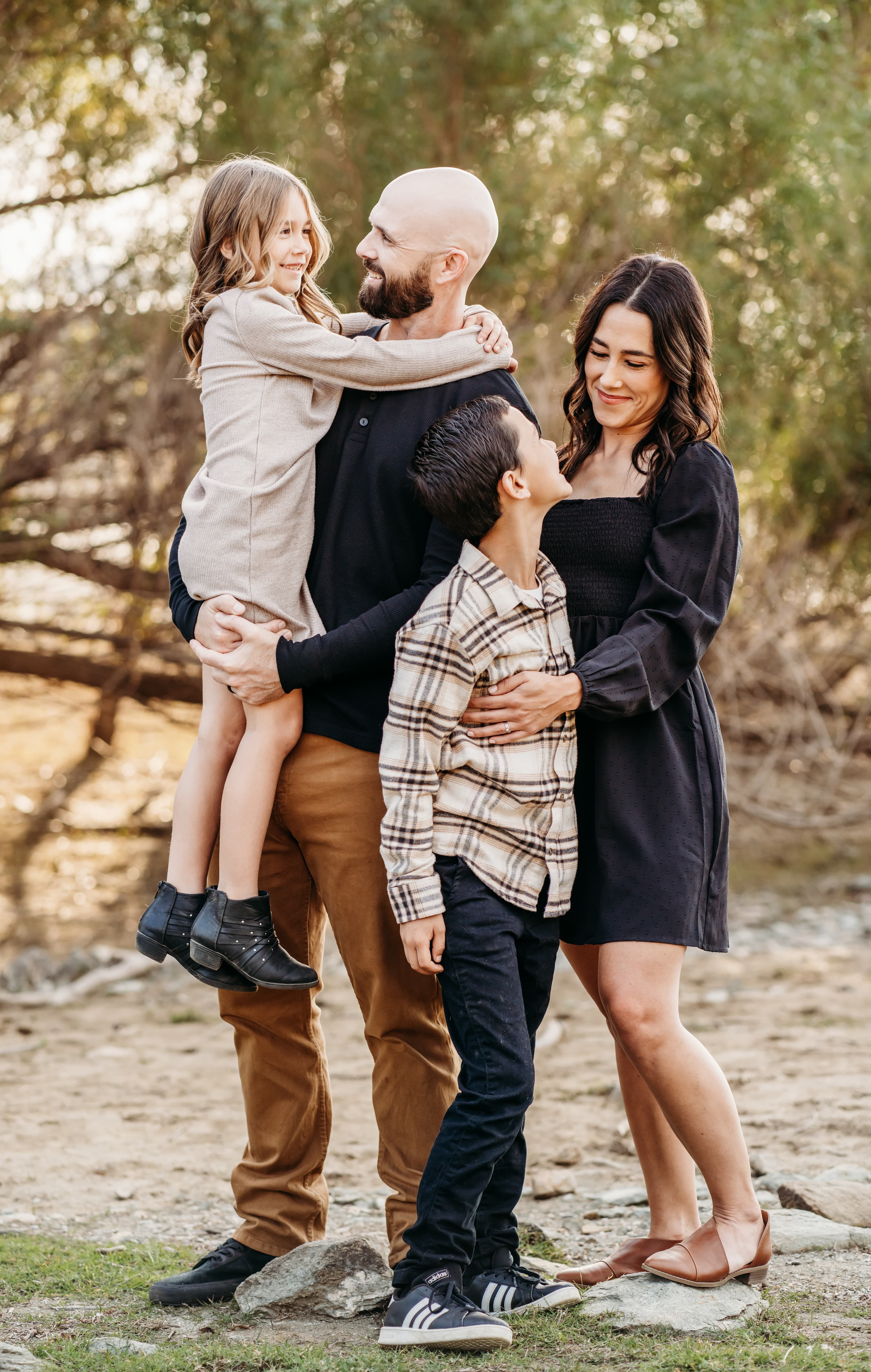 Father holds his daughter and mother embraces her son in a riverside family portrait