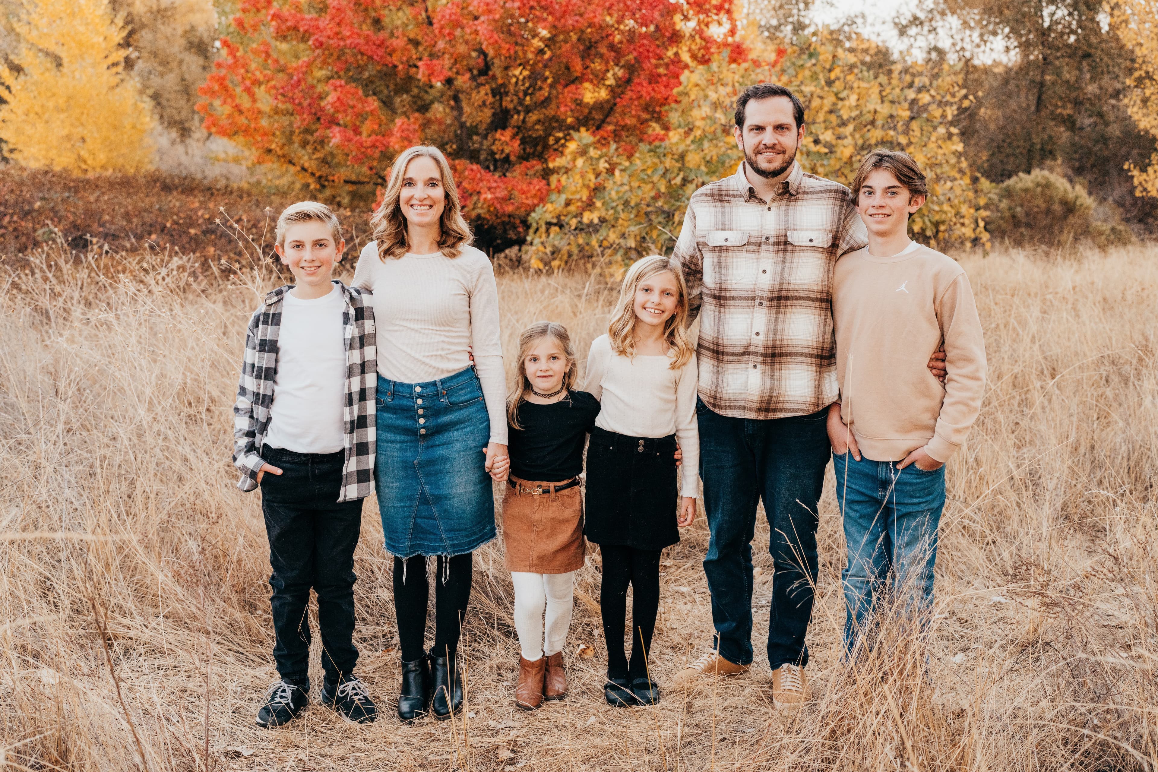 Family of six gathers together in front of a vivid red and orange fall tree