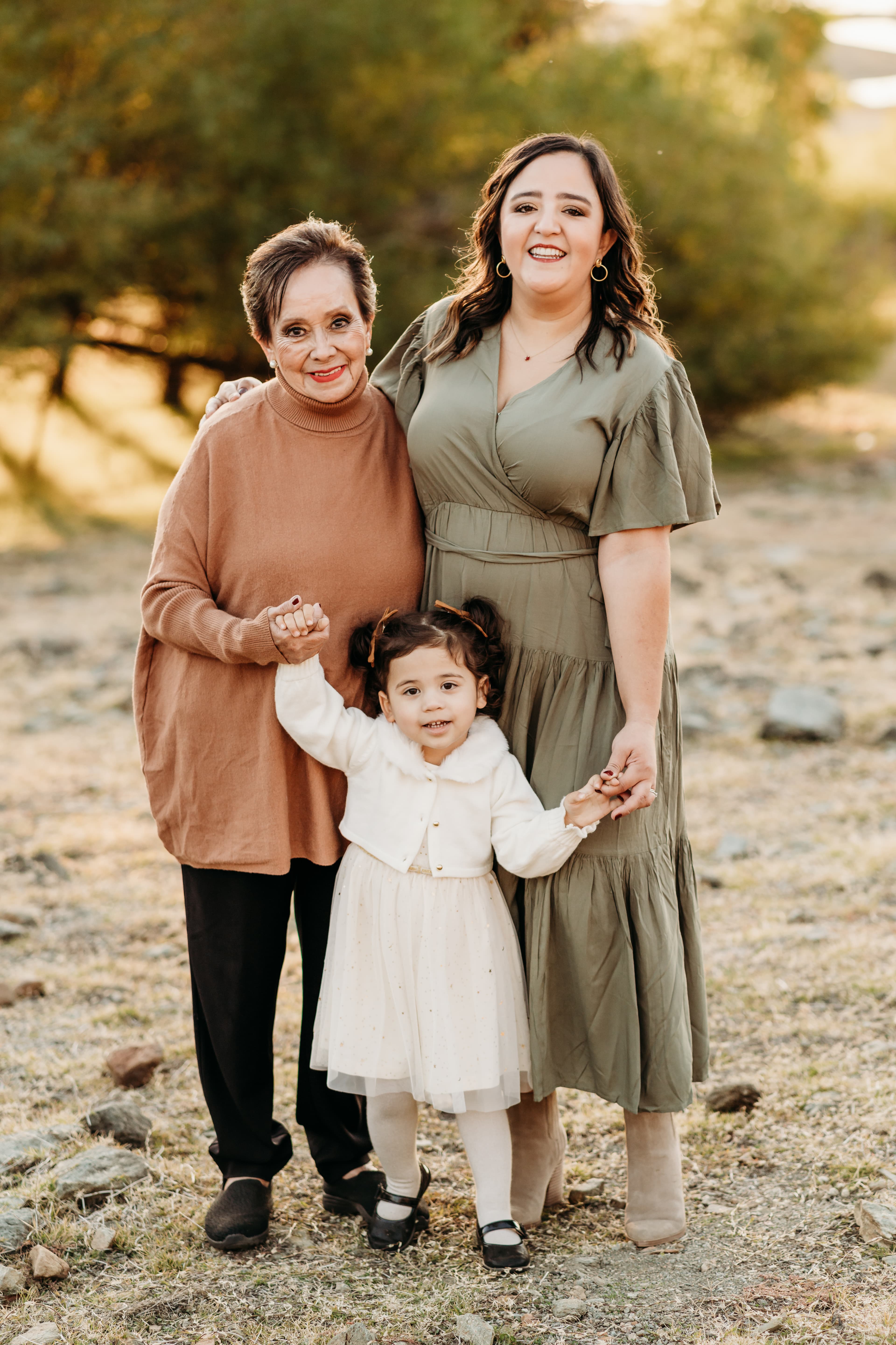 Grandmother, mother, and granddaughter smiling together outdoors, holding hands