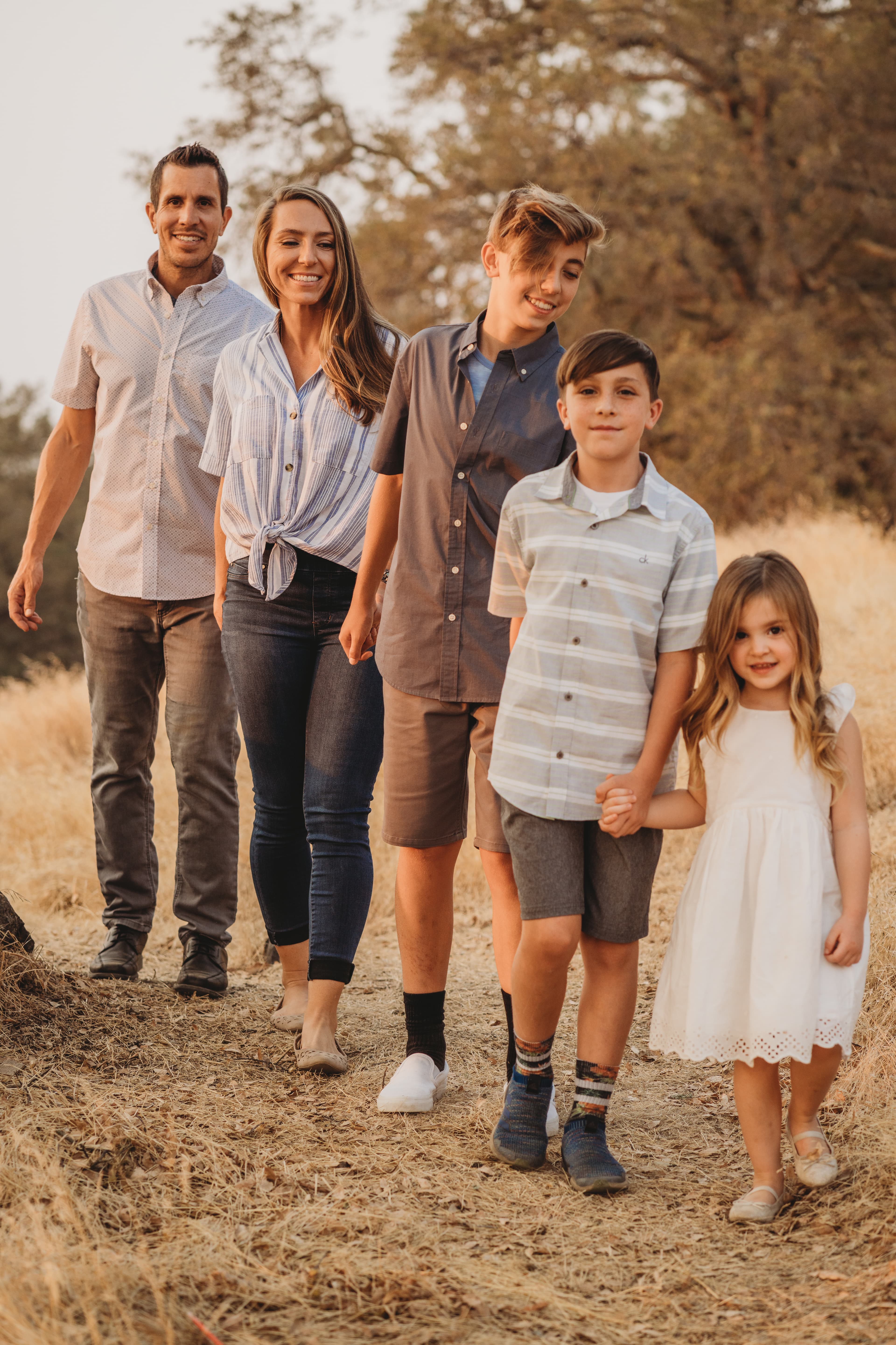 Family of five walks hand in hand along a dirt path through dry golden grass