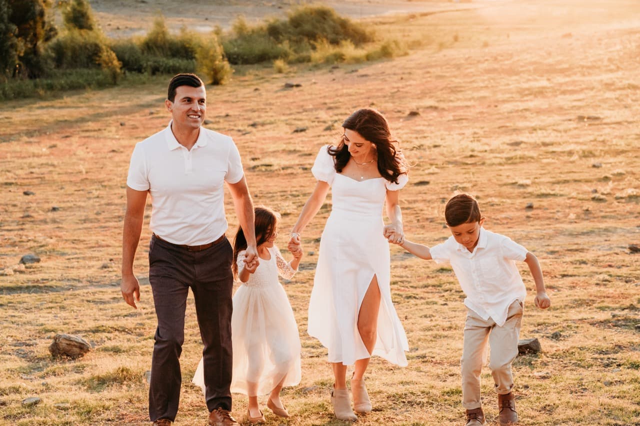 Family of four in white walks hand in hand across a sunlit golden field