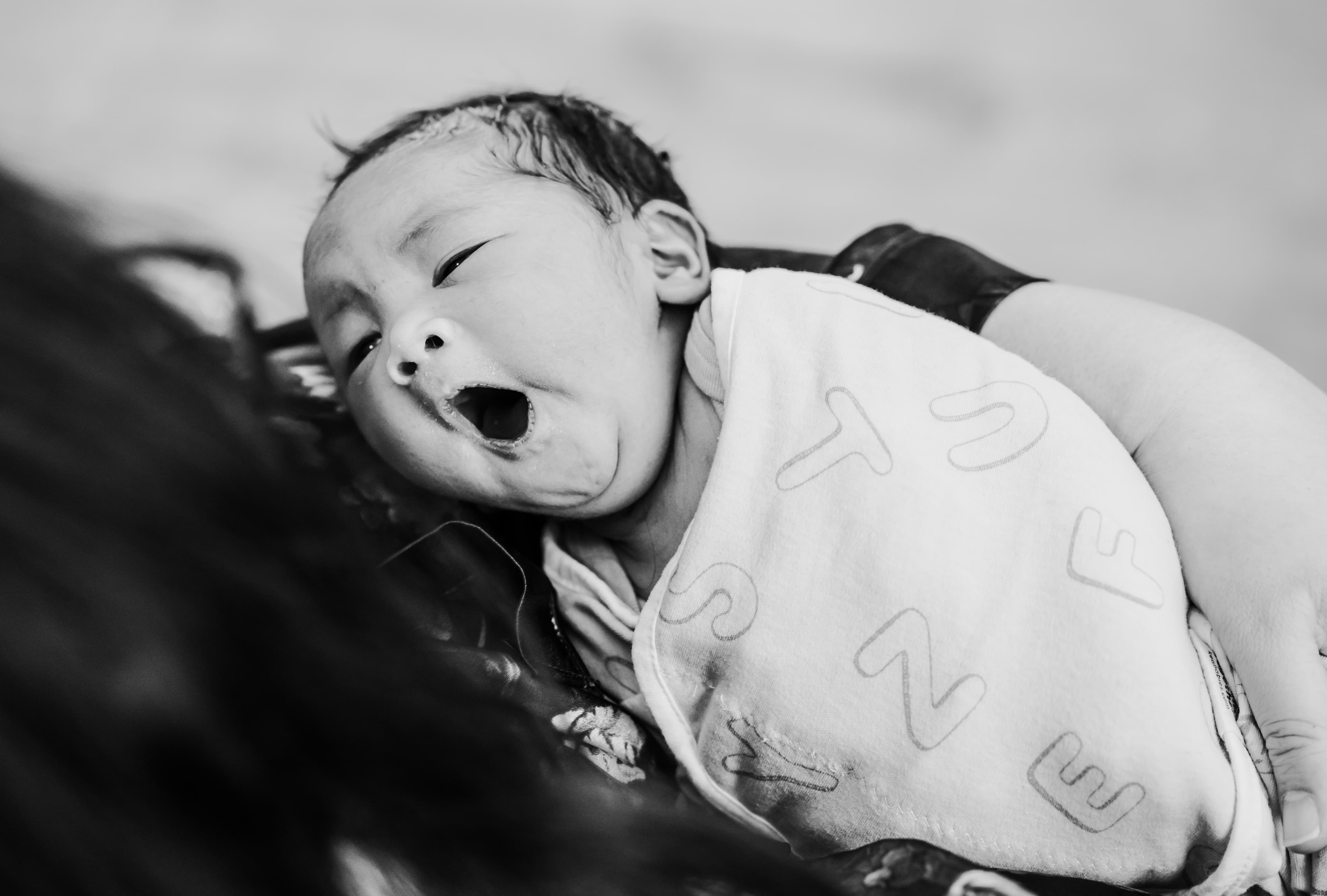 Black-and-white close-up of a newborn yawning against a parent's shoulder