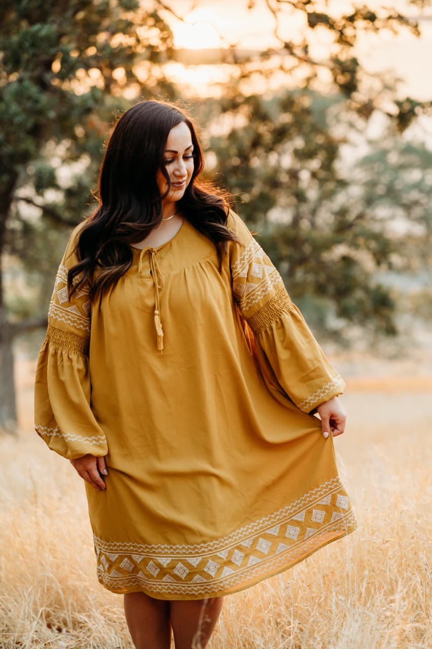 Woman in a mustard bohemian dress smiles in a golden sunset field