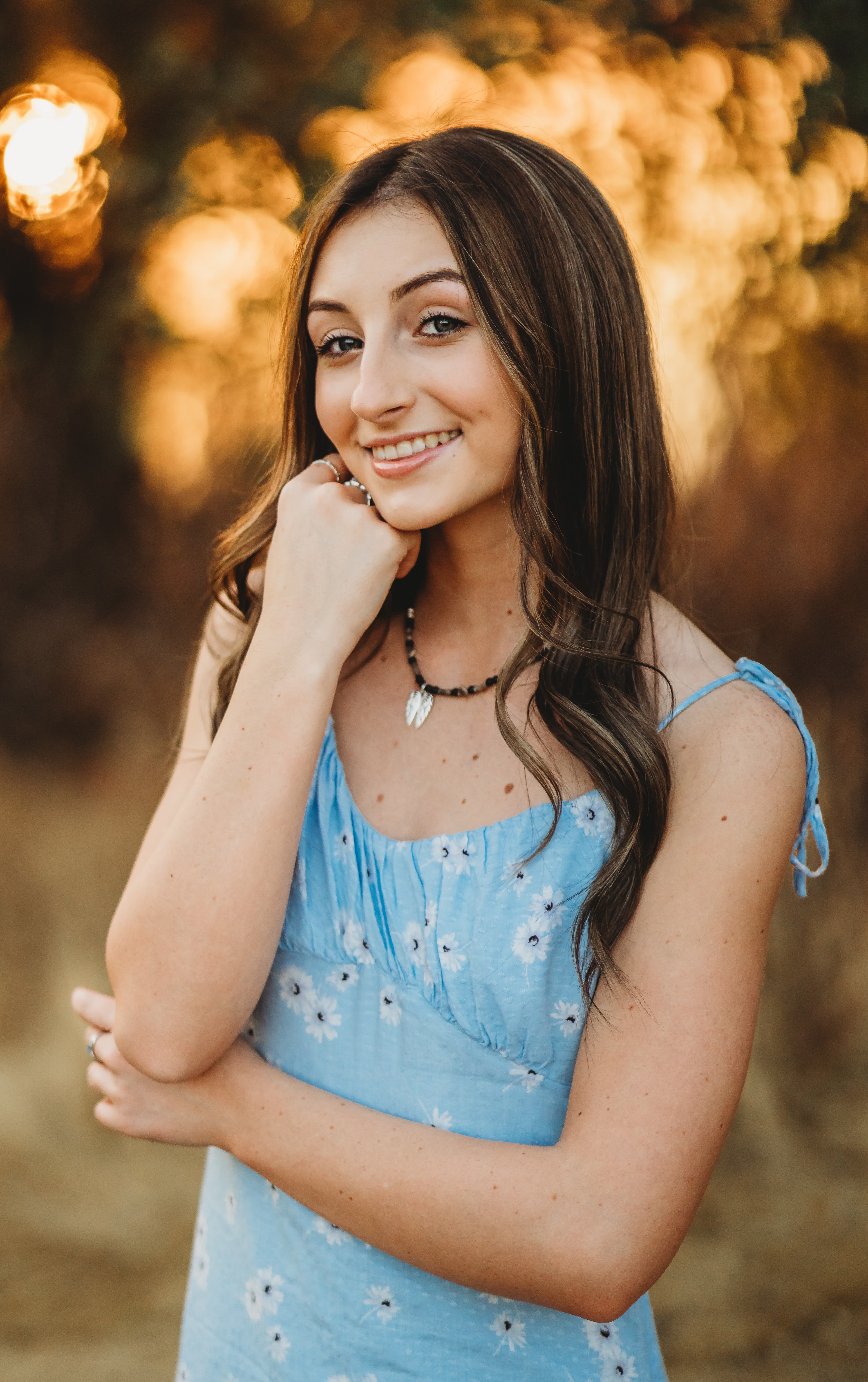 Teen girl in a blue floral dress smiling with her chin on her hand