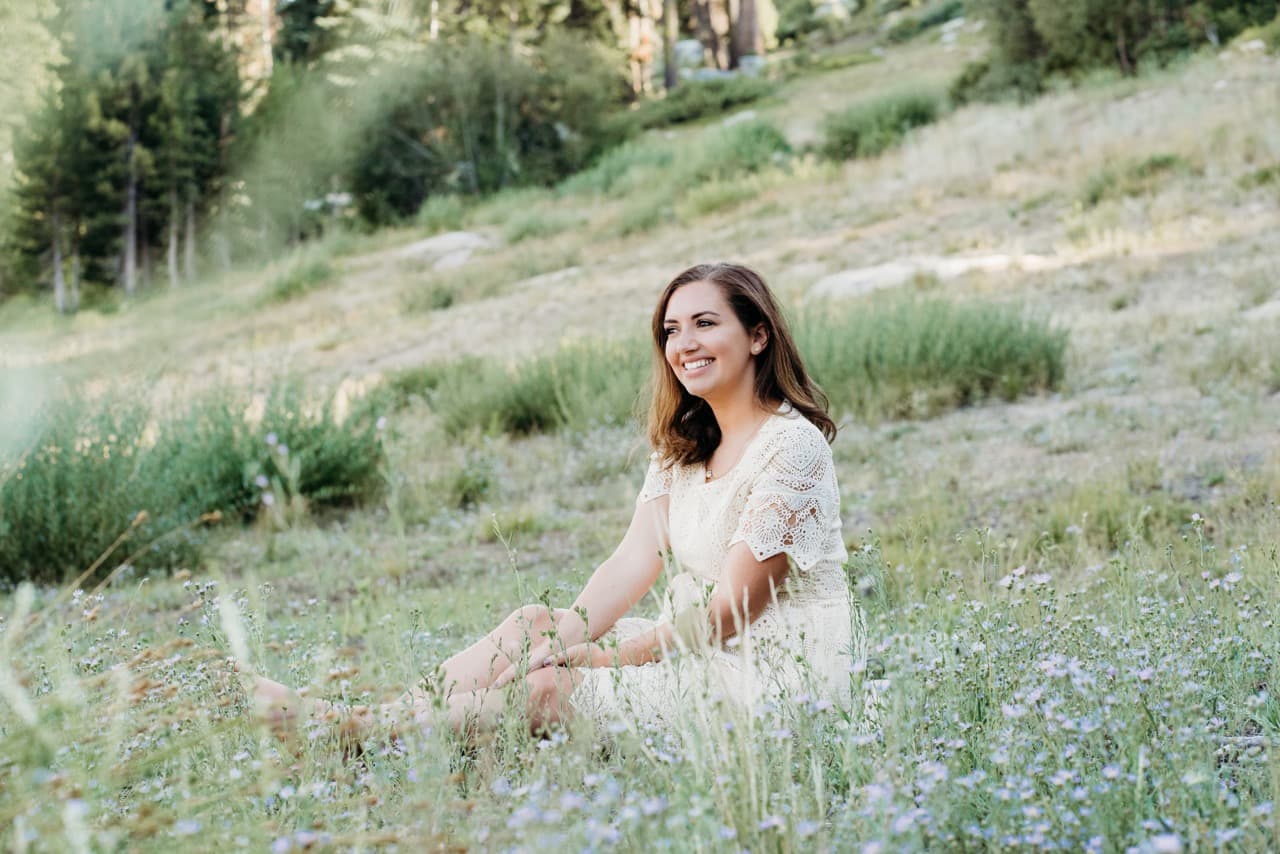 Woman in a cream lace dress smiling in a mountain wildflower meadow
