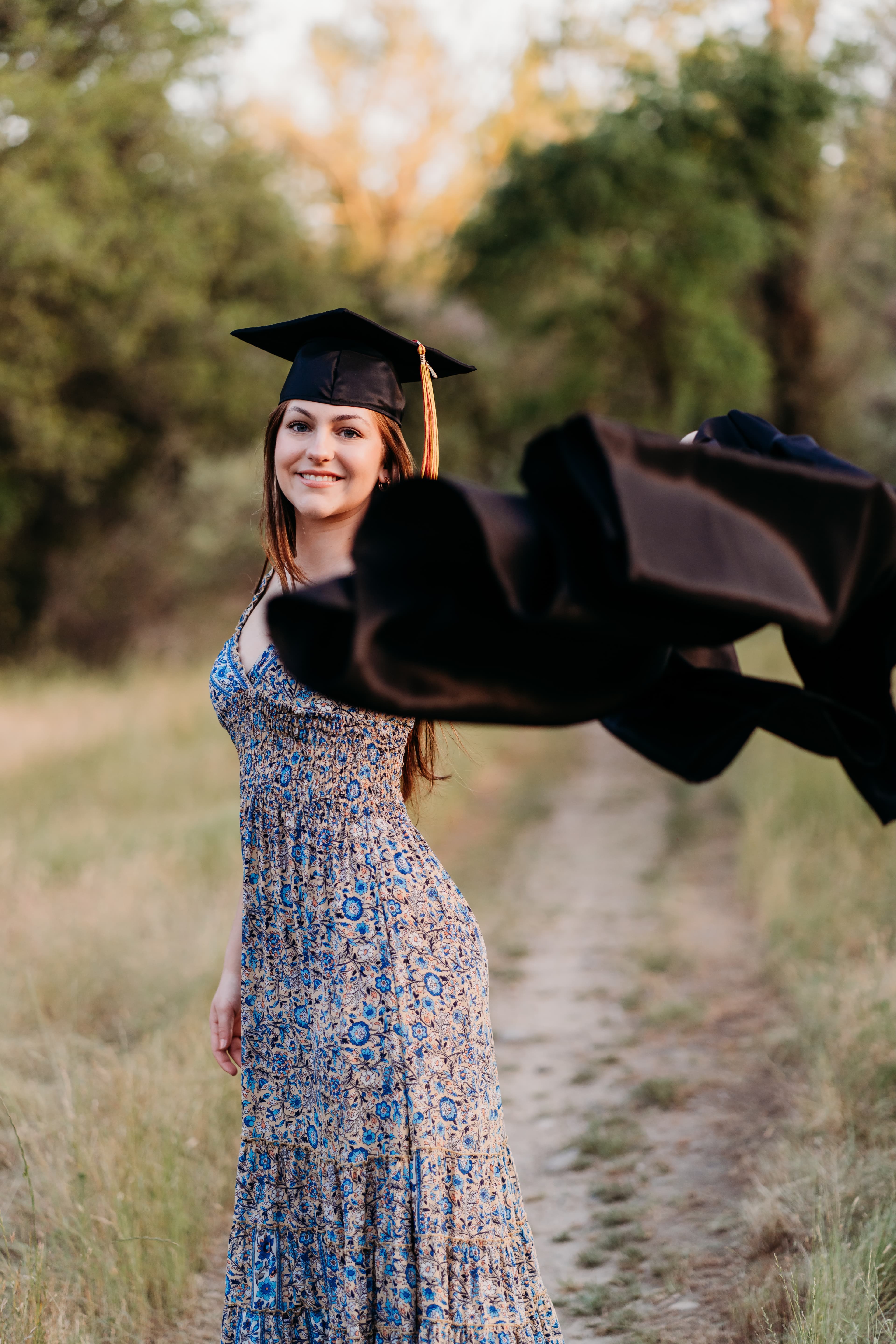 Graduate tosses her cap and gown into the air on a path through a golden field