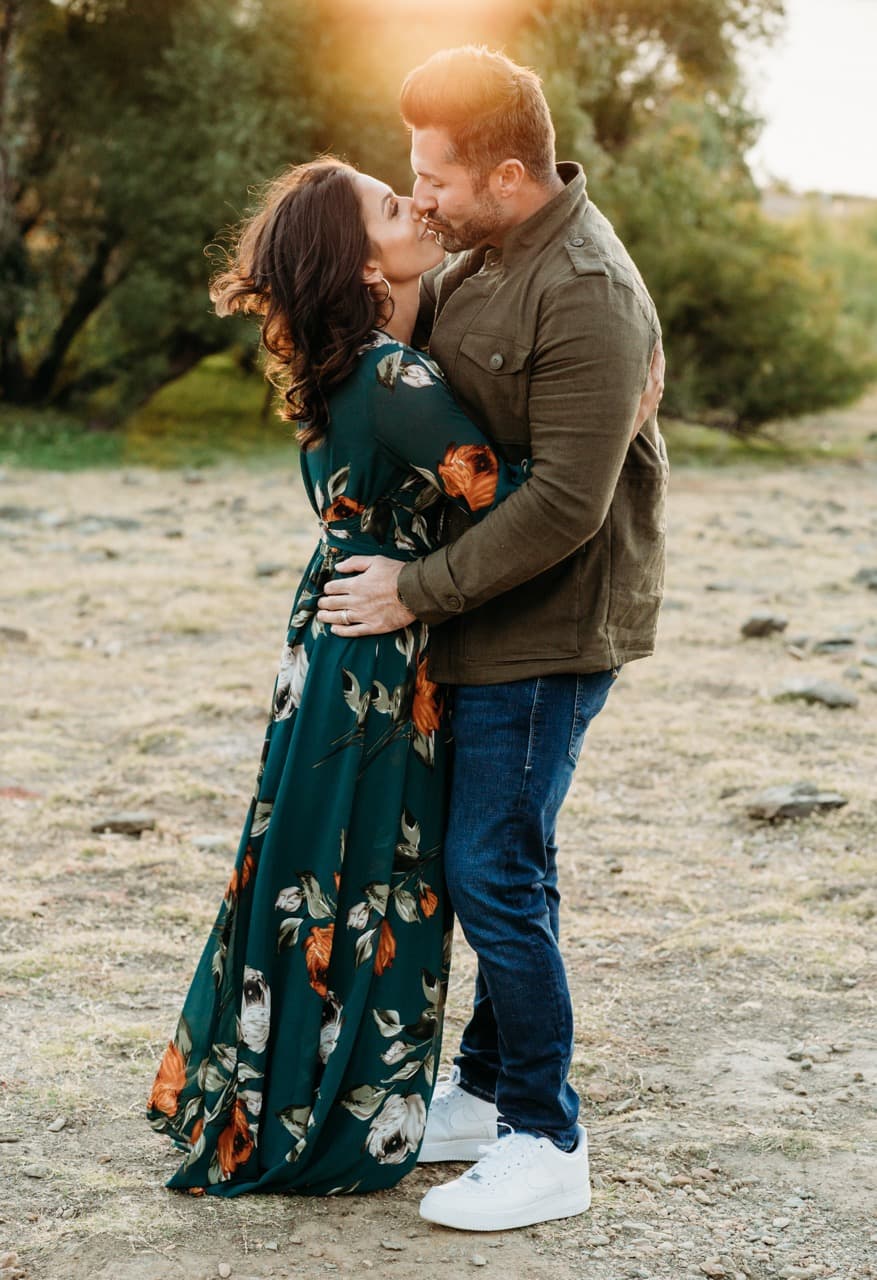 Couple kisses on a dirt path at sunset, she in a green floral dress