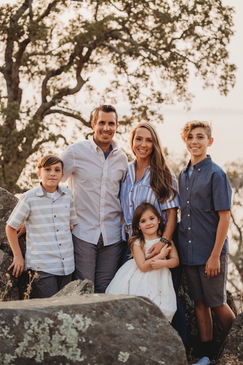 Family of five poses on granite boulders overlooking a lake at sunset